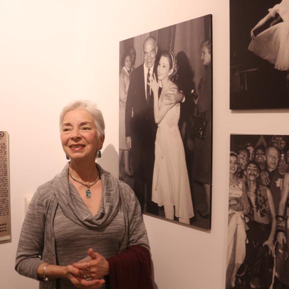 Old lady standing by photos on the wall smiling