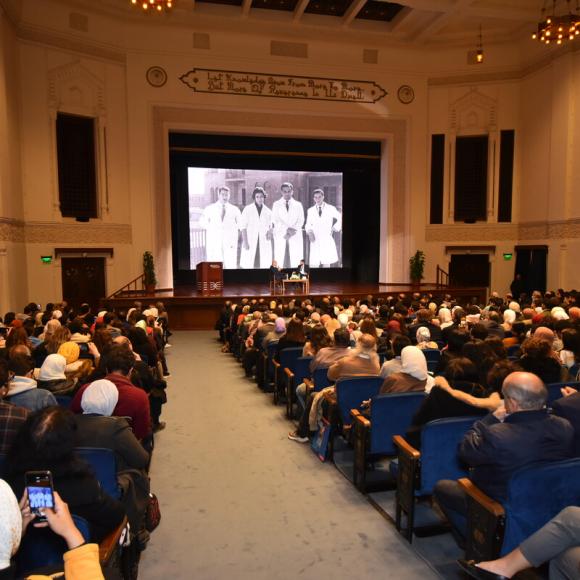 People sitting in a hall listening to people on stage 