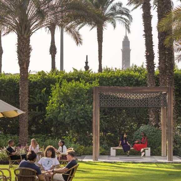 A group of international students sitting around a table in a garden with greenery and palm trees around them