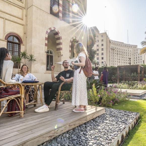 a group of girls and boys sitting at a table outdoors talking together