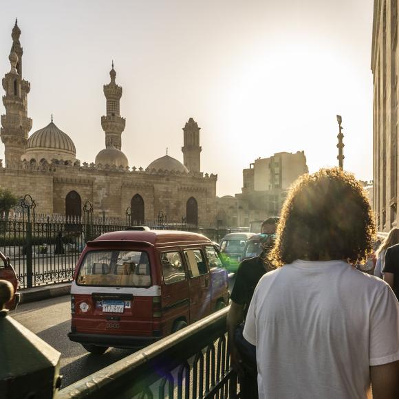 Students walking in the streets of Cairo with cars and a mosque in the background