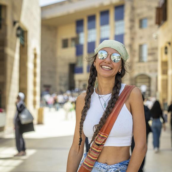 Girl wearing sunglasses and a head bandana smiling on campus