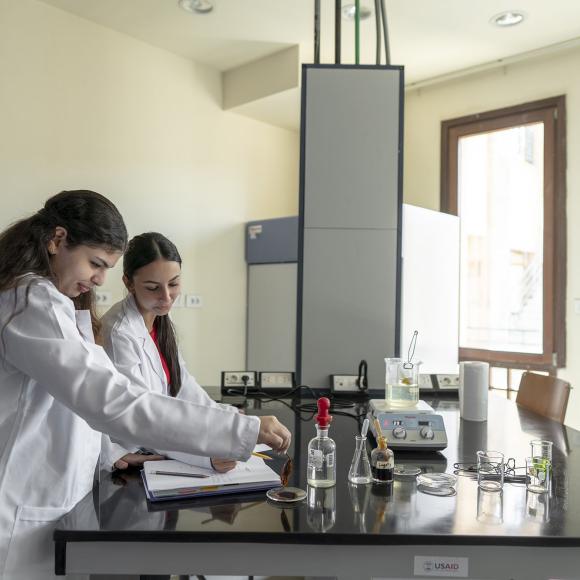 two girls wearing white lab coat conducting an experiment in a lab