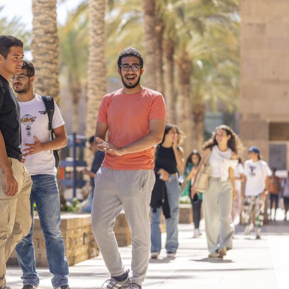 Three male students laughing, talking and standing next to palm trees on campus
