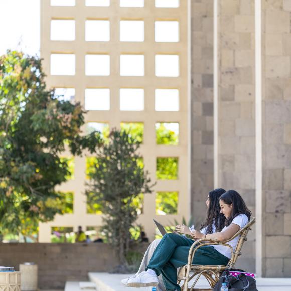 Two female students smiling and sitting on chairs on stairs.