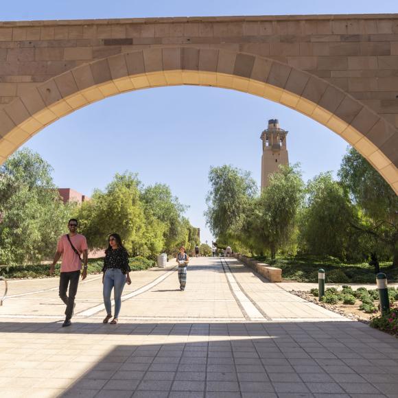 A male and female student talking and walking under an arch.