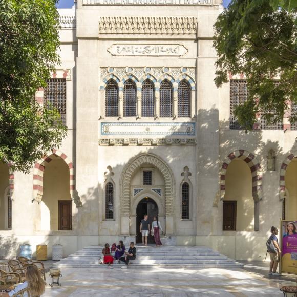 An old islamic design building with three flags on the top and people walking outdoor