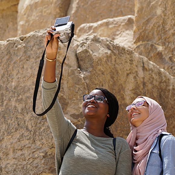 Two girls by the pyramids taking a selfie using a camera