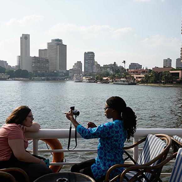 A girl taking picture of another girl using a camera by the nile