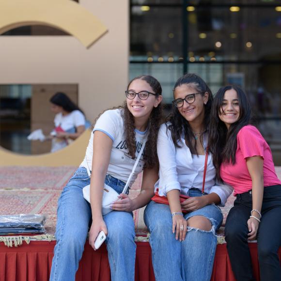 three smiling girls sitting on a stage in AUC plaza