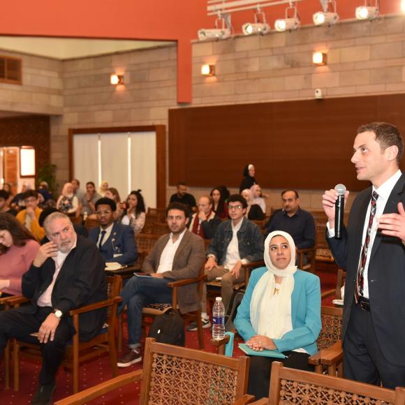 Audience sitting in an event and a man is talking in a microphone