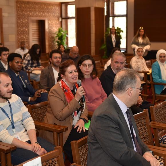 Audience sitting in an event and a woman is talking in a microphone