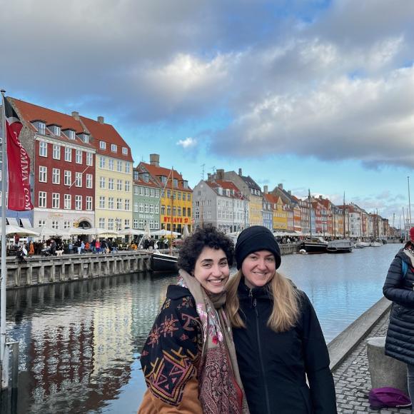 Two female students standing by a lake and colored houses