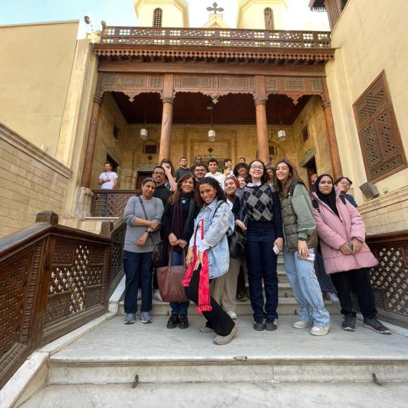 A group of students stands in front of a beige building