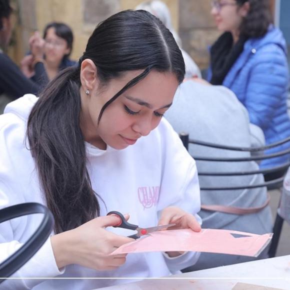 A student uses scissors to cut pink craft paper