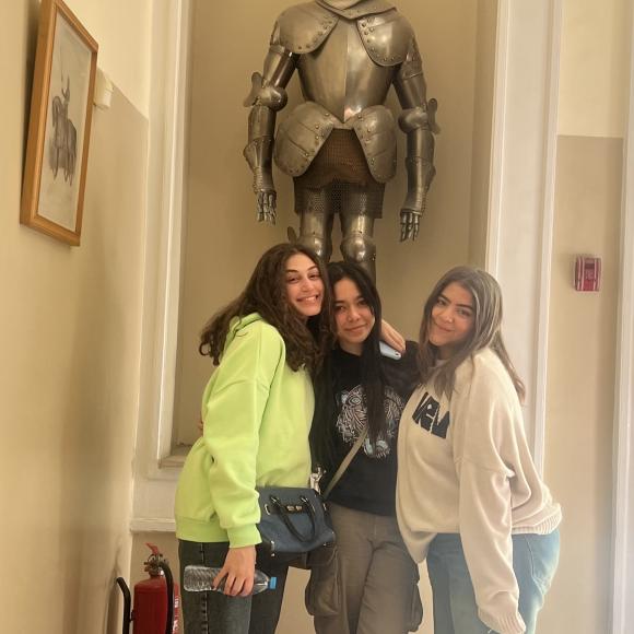 A group of three students pose in front of a suit of armor