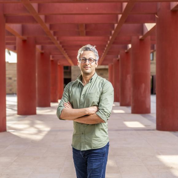 A male wearing glasses is standing next to red pillars