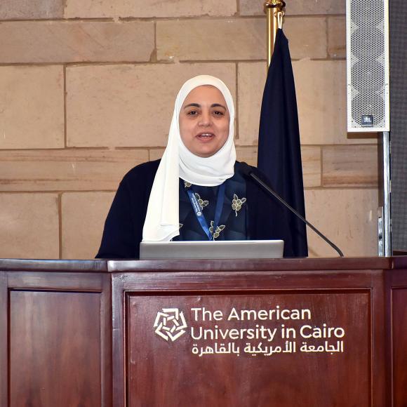 a veiled woman wearing a white scarf giving a speech