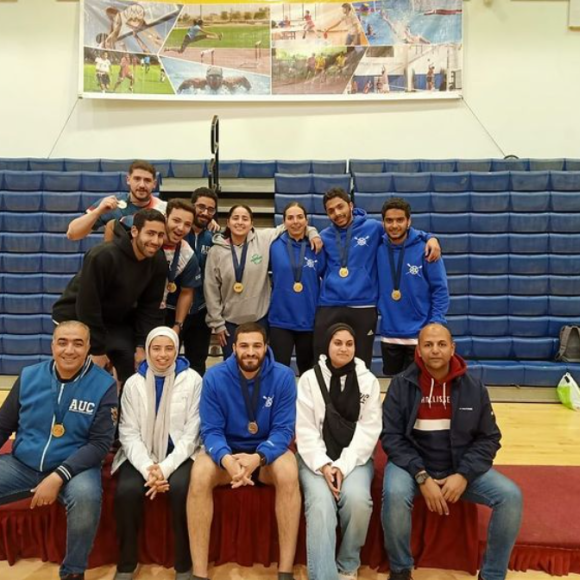 A group of male and females standing and sitting together in a sports court, they are wearing medals
