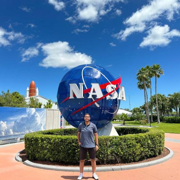 A male student standing in front of the NASA globe, there is a rocket behind them