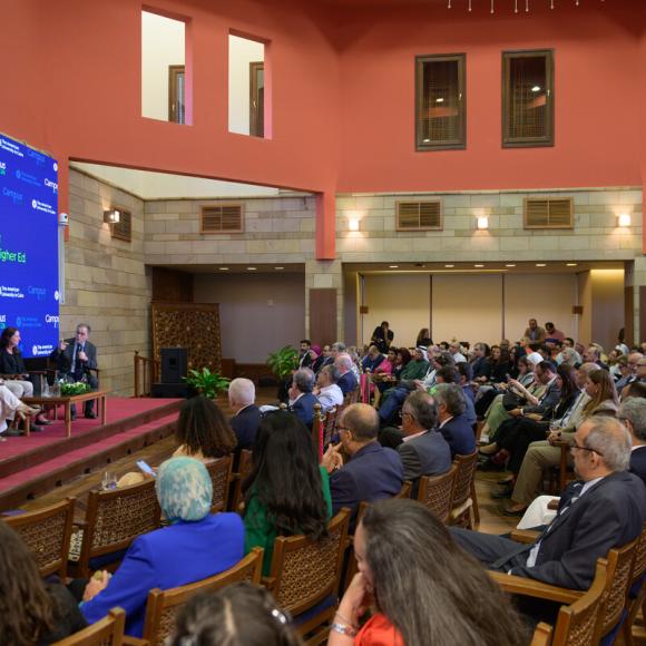 Audience watching two men and two women sitting on a podium. Text: Campus 2026 Groundbreaking. Building for the Future of Higher Ed. The American University in Cairo