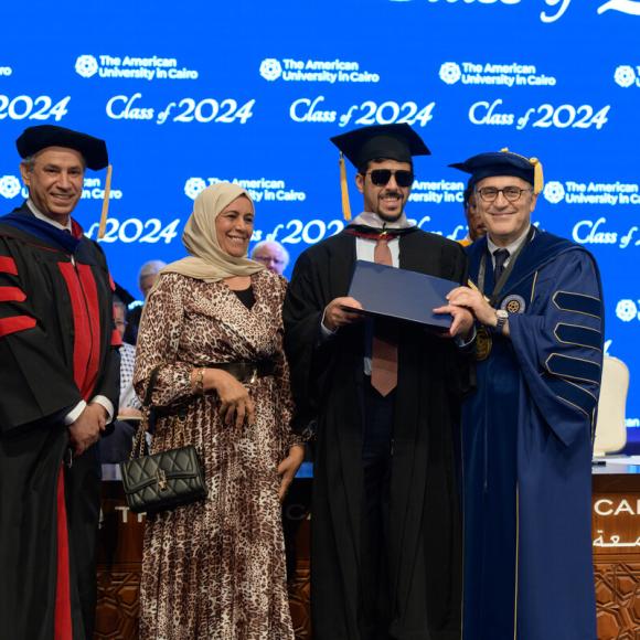 Three males and a woman standing together, the males are dressed in caps and gowns. Text: The American University in Cairo. Class 0f 2024