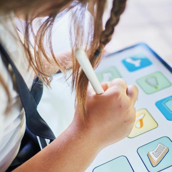 a young girl holding a pen in her hand and working on an ipad