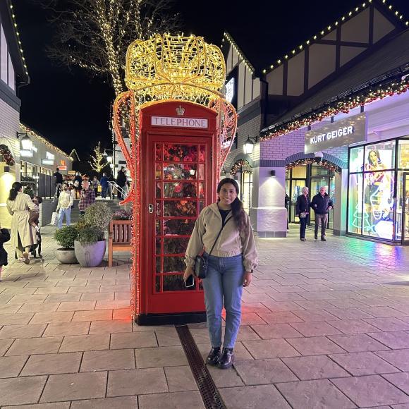 A female is standing and smiling in front of the red English telephone booth