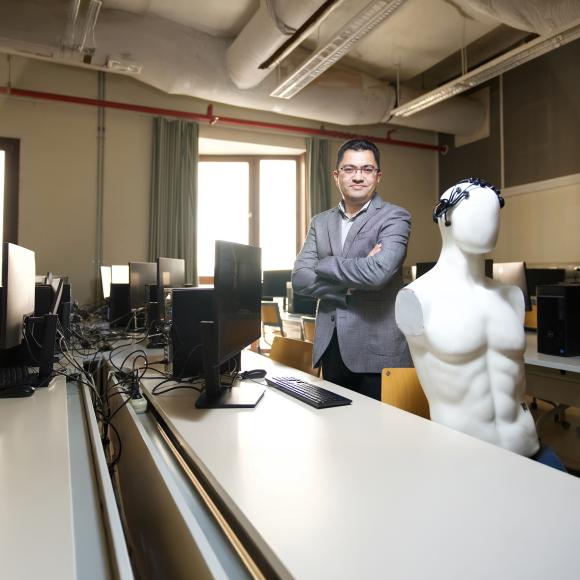 a professor wearing a grey suit with short black hair standing in a computer lab room