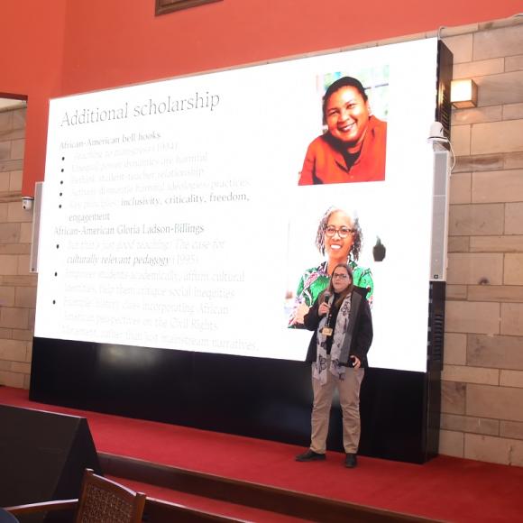 A woman is talking into a microphone. There is a screen behind her that reads: Additional Scholarships
