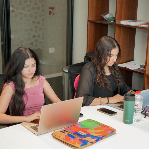 two students sitting next to each other in front of their laptops