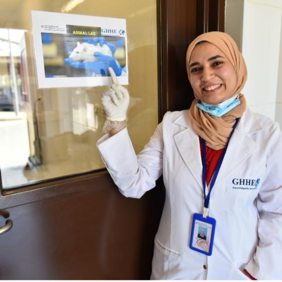 a veiled woman wearing a yellow scarf and a white coat pointing to a door