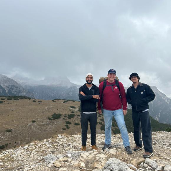 Three males are standing on a mountain top