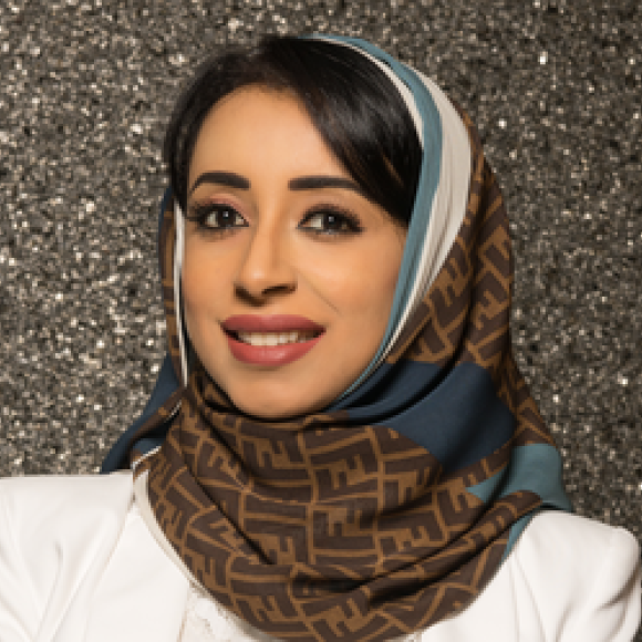 a headshot of a woman wearing a head scarf and a white blazer