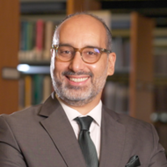 a bold man with grey beard wearing a brown suit and eye glasses
