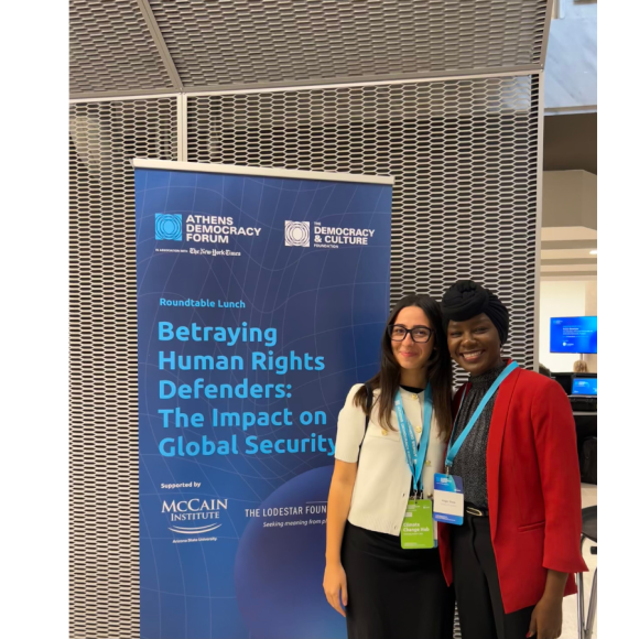 Two participants at the forum standing in front of a banner