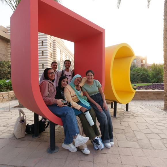 Males and females are sitting and smiling on a big letter U