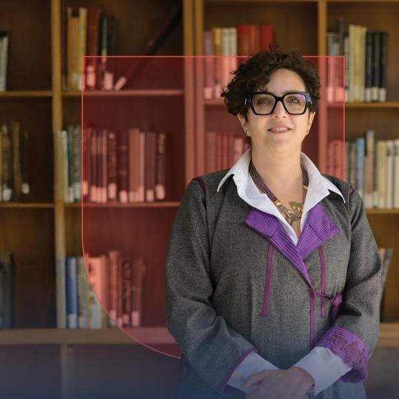 A female is standing and smiling. There is a bookshelf behind her.