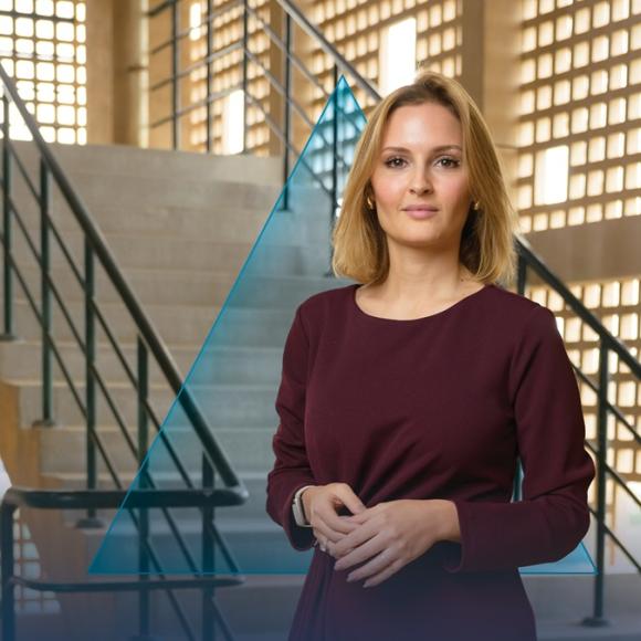 A female is standing and smiling. There are stairs behind her