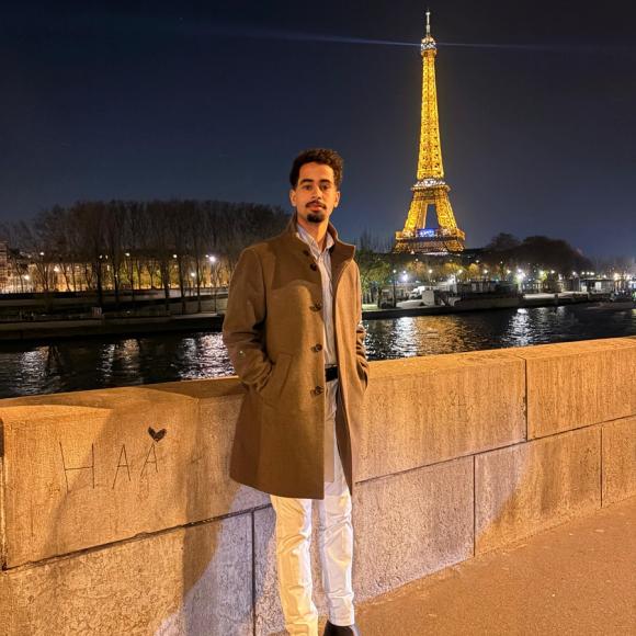 A male is standing. The Eiffel Tower is behind him