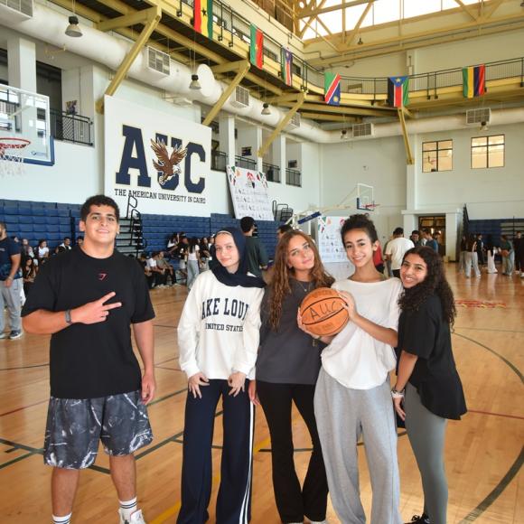 Males and females are standing in a basketball court. They are smiling