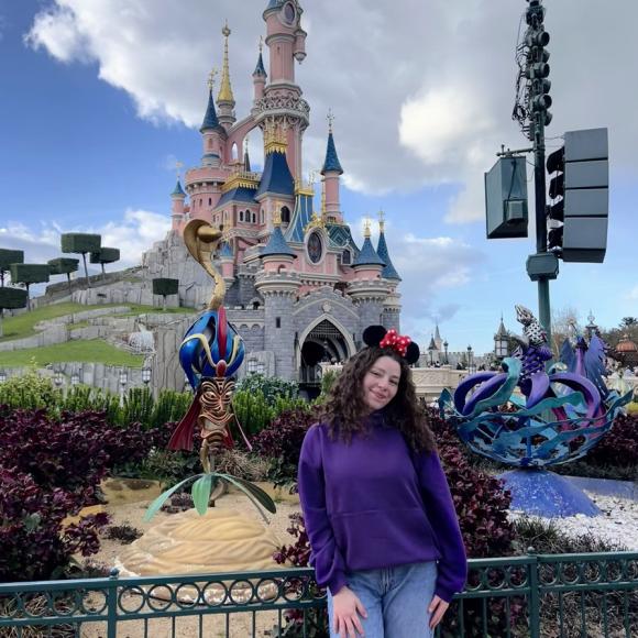 A female is standing and smiling in front of the Disneyland castle