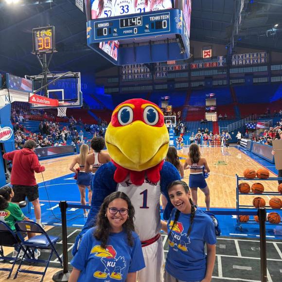 Two females are standing next to a mascot of a big red bird